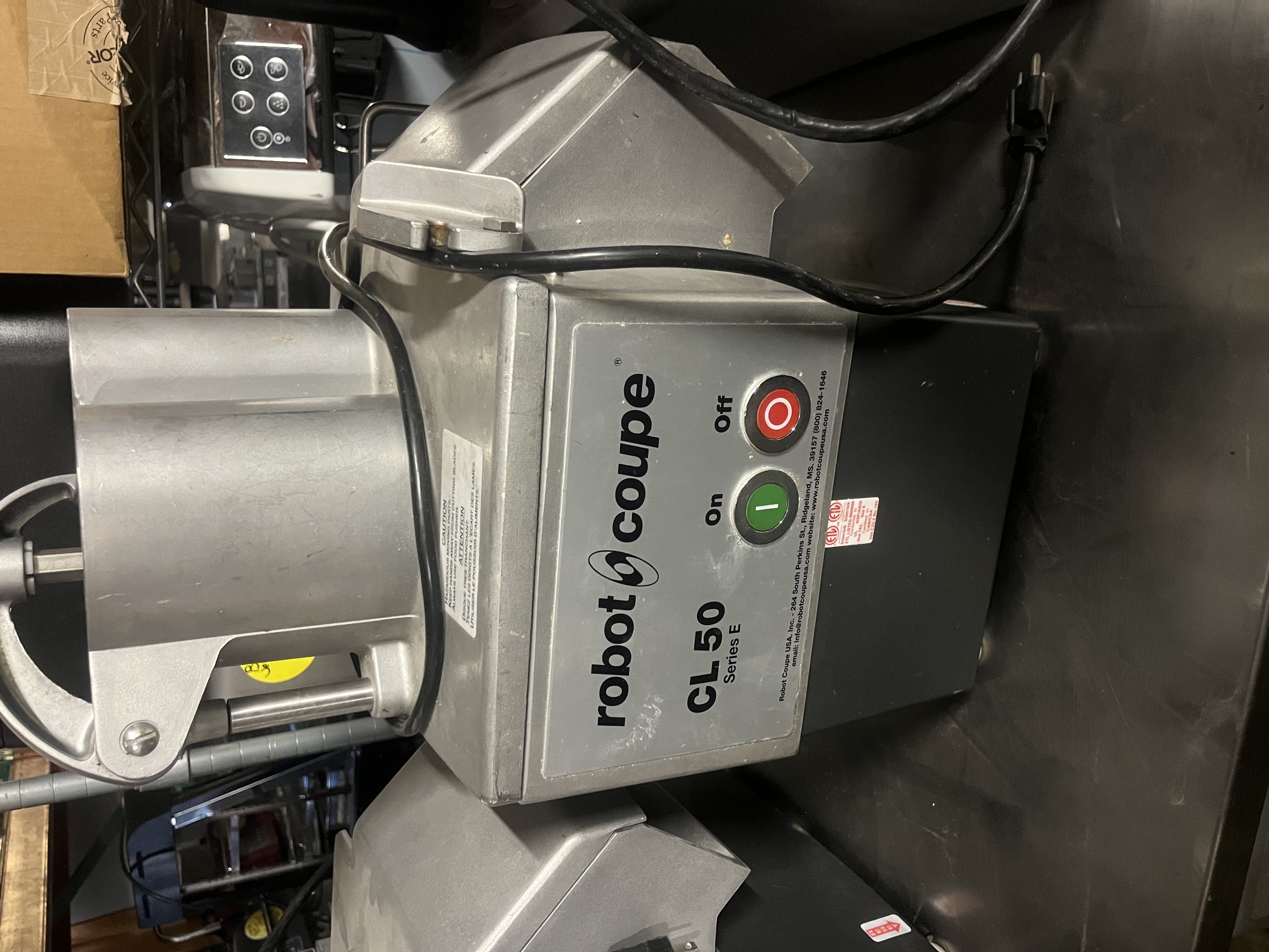 Robot Coupe CL 50 Series E commercial continuous-feed food processor on stainless steel table, showing front panel with brand logo, model number, and green On / red Off push buttons