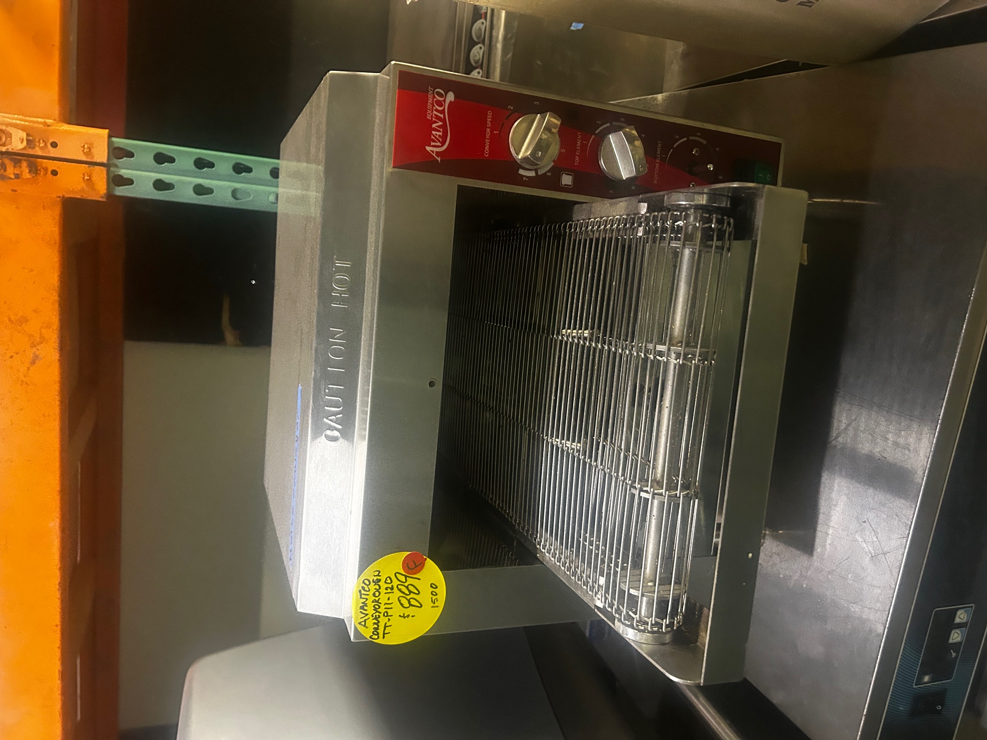 Avantco TT-P11-120 countertop conveyor oven on a shelf showing front view with conveyor belt, control knobs, and yellow price sticker