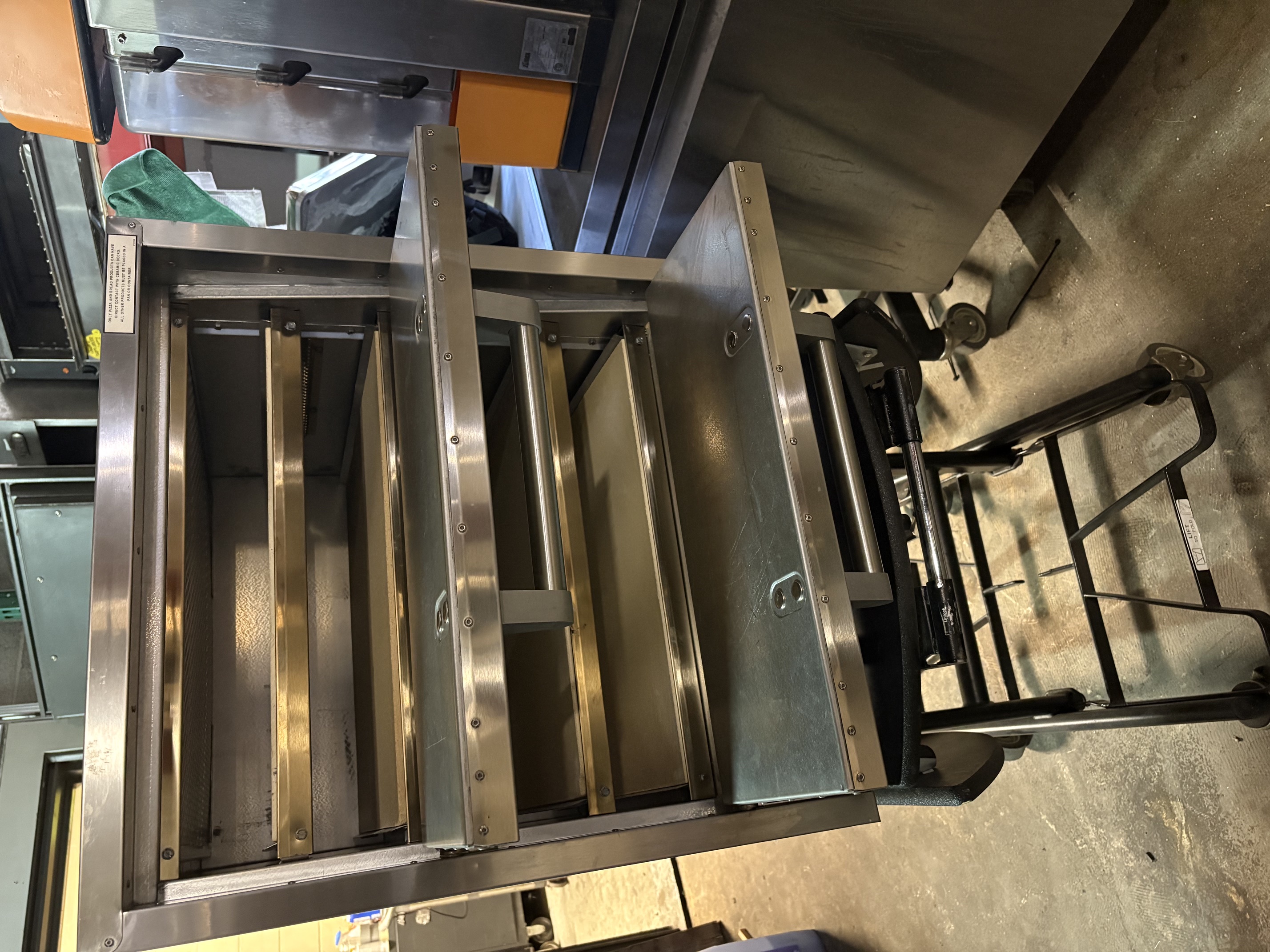 Standex P44S four-deck electric countertop pizza oven shown open with all four stainless steel decks visible, sitting on a mobile cart in a warehouse