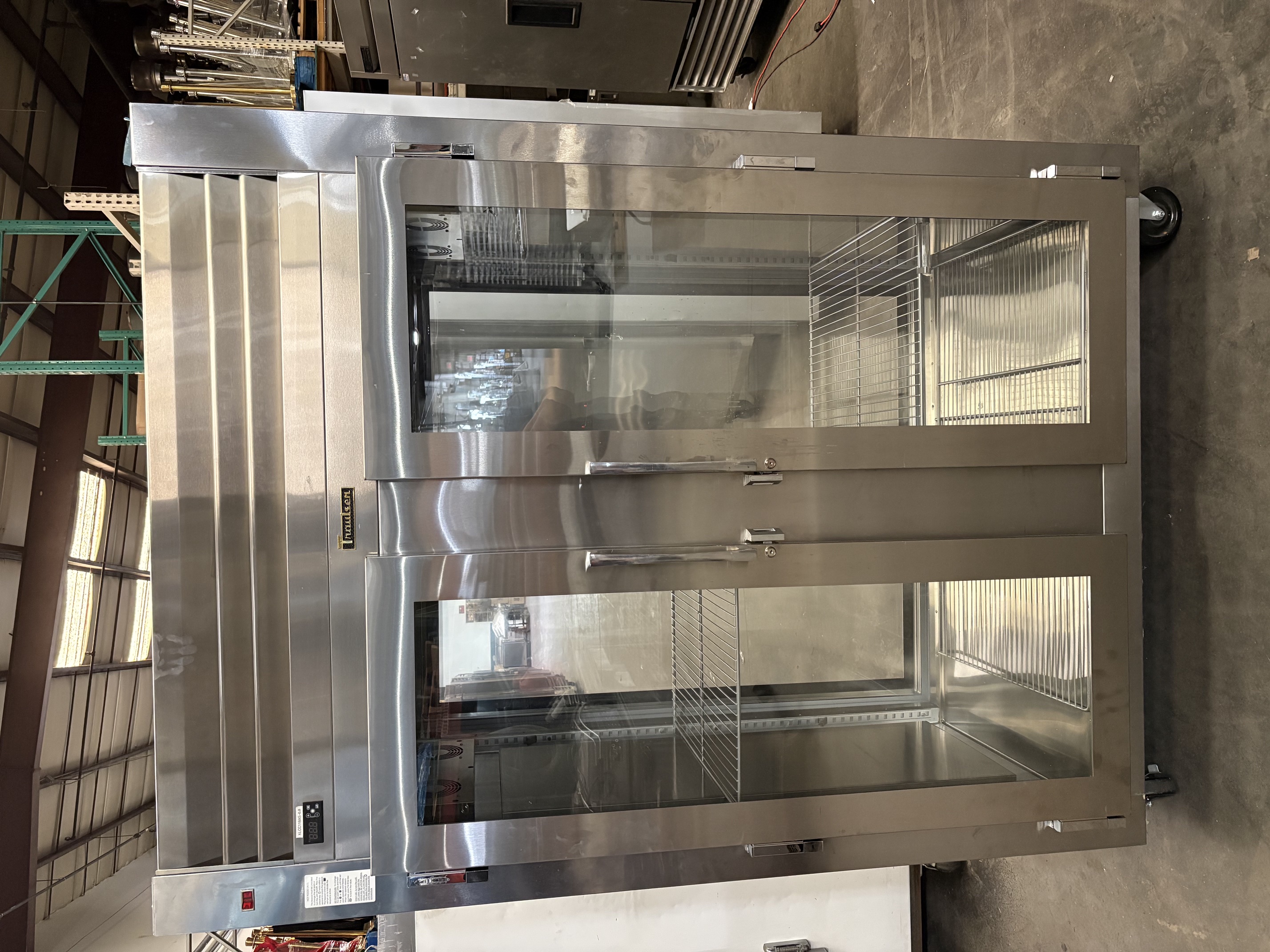 Front view of Traulsen AHF232WP-FHG two-section pass-through heated holding cabinet with full-height glass doors showing stainless steel exterior, adjustable wire shelves, digital temperature control, and casters in warehouse setting
