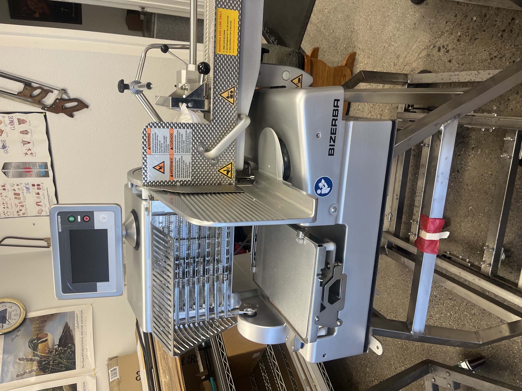 Front view of Bizerba VSI F slicer showing digital touchscreen, blade guard, carriage, and safety labels on stainless steel stand
