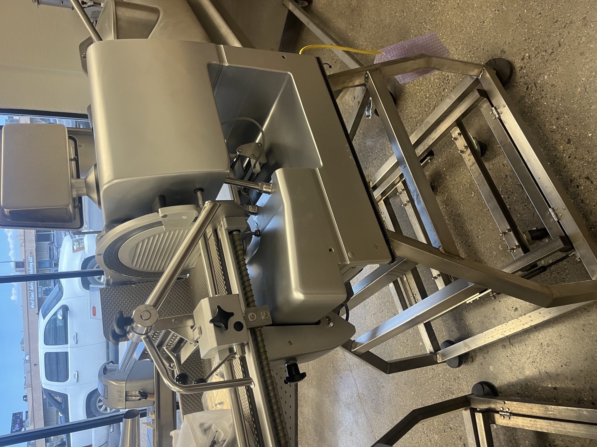Side angle view of Bizerba VSI F slicer showing carriage arm, blade, and product deflector on rolling stainless steel stand
