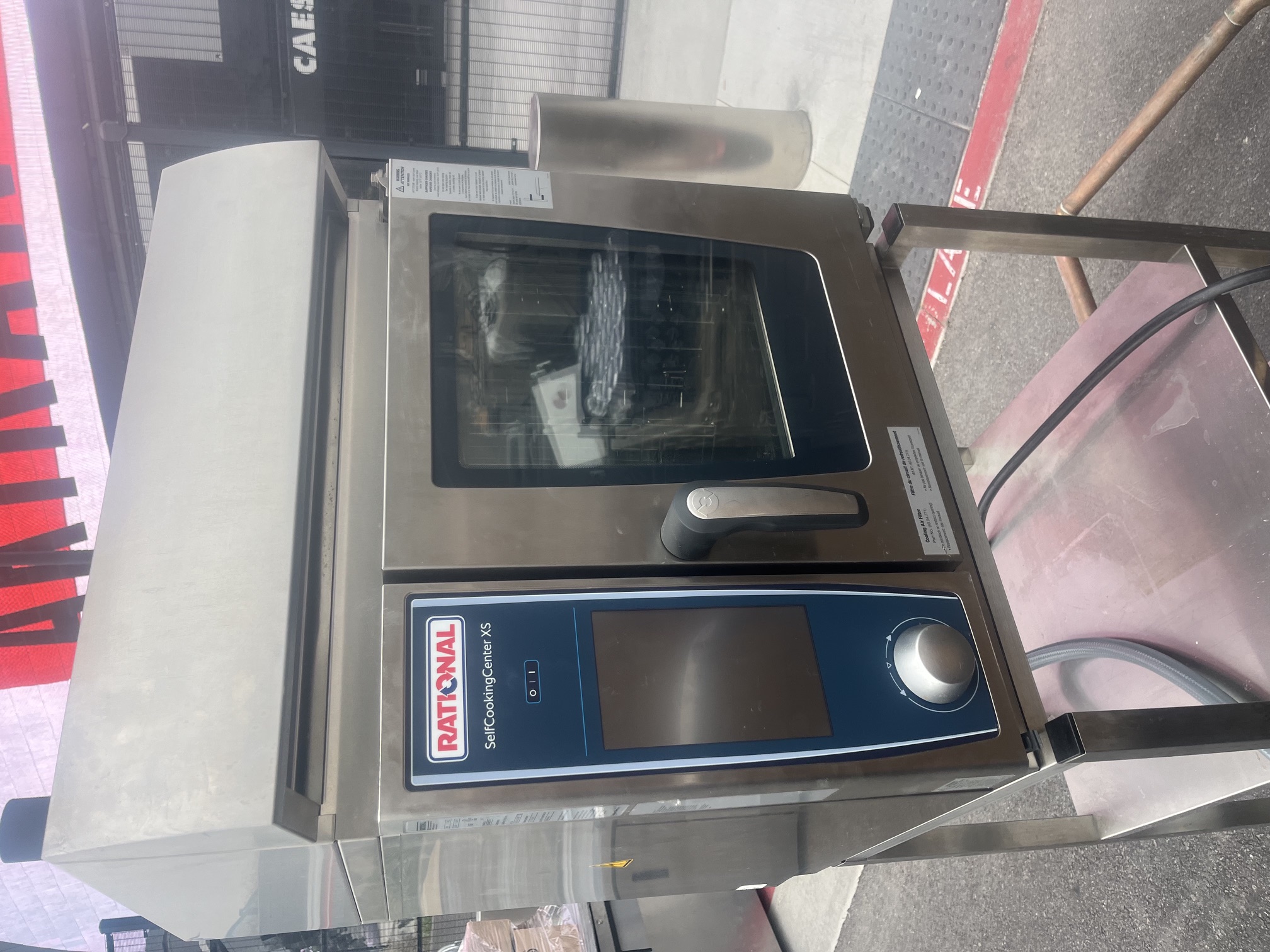 Rational SelfCookingCenter XS combi oven on stainless steel stand, front-angle view showing glass door and blue control panel