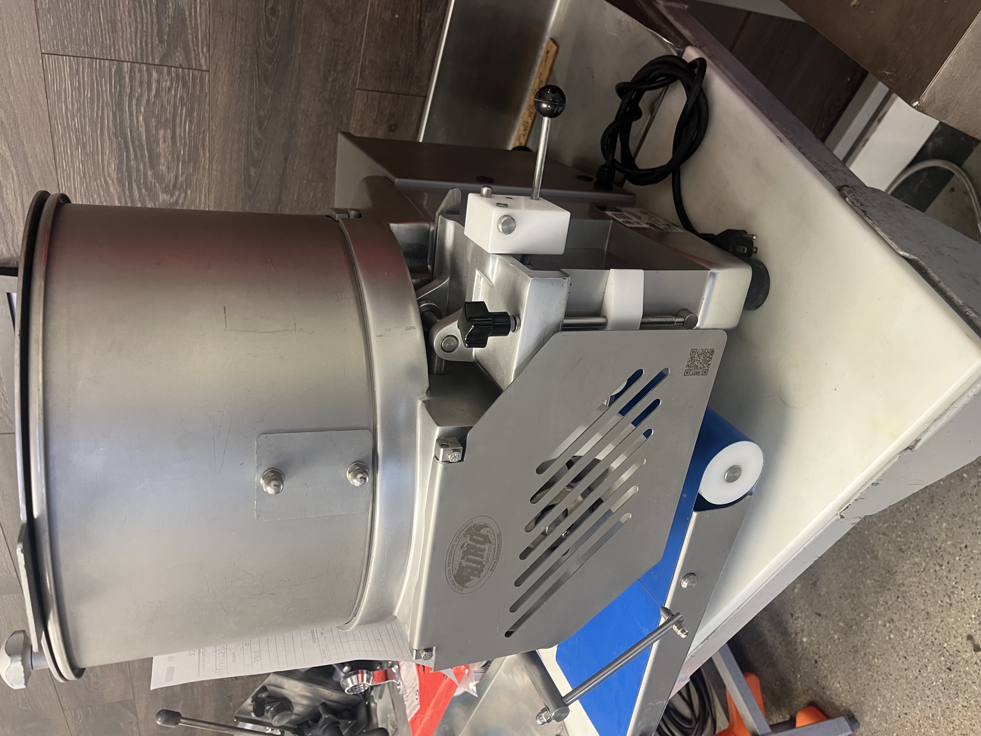 Rear/side view of Biro F2000PLUSB patty former showing Biro logo badge, ventilation grille, power cord, and blue conveyor belt