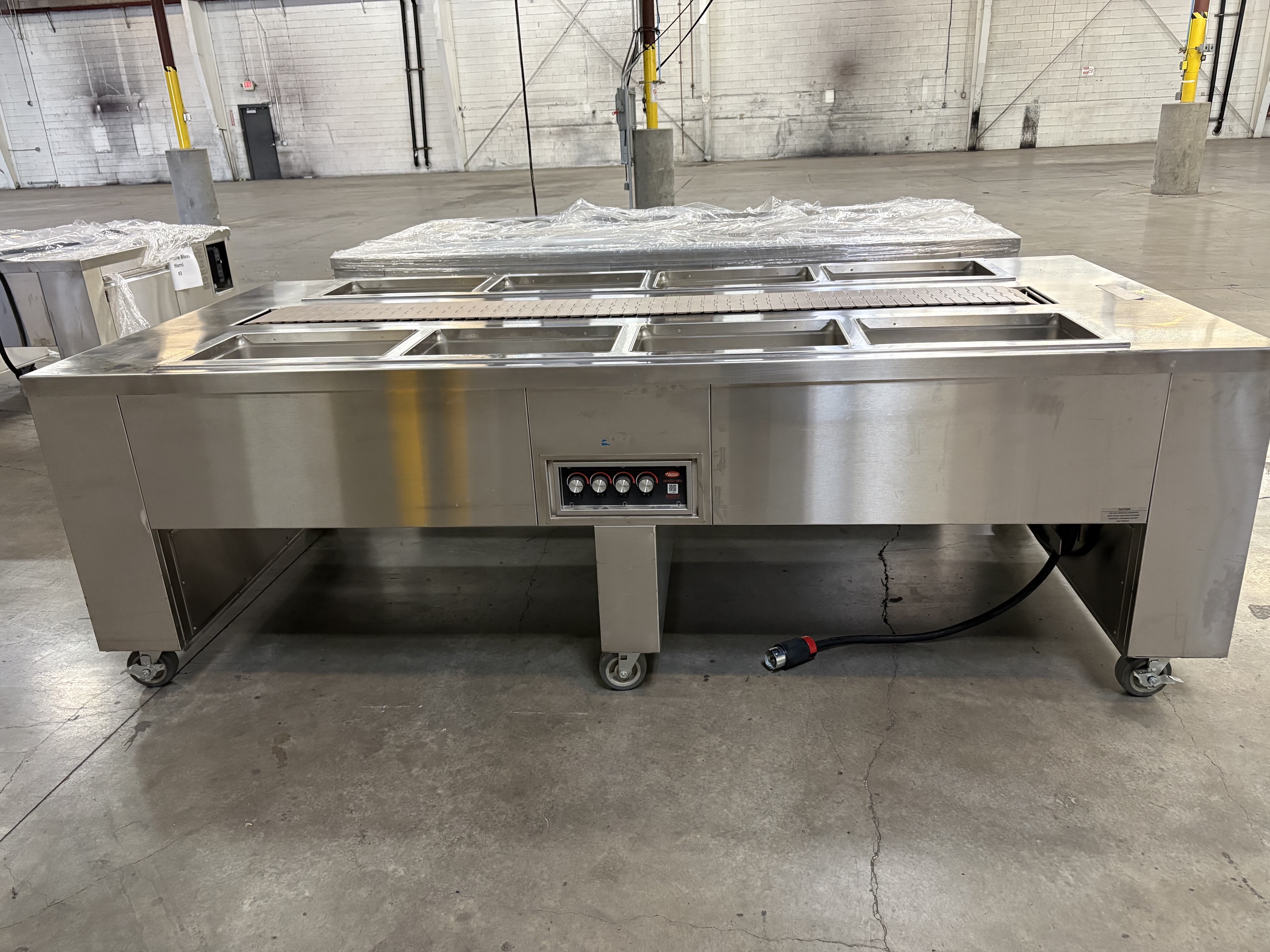 Front view of Gates 8-foot tray make-up conveyor showing 8 Hatco heated wells and stainless steel construction on casters