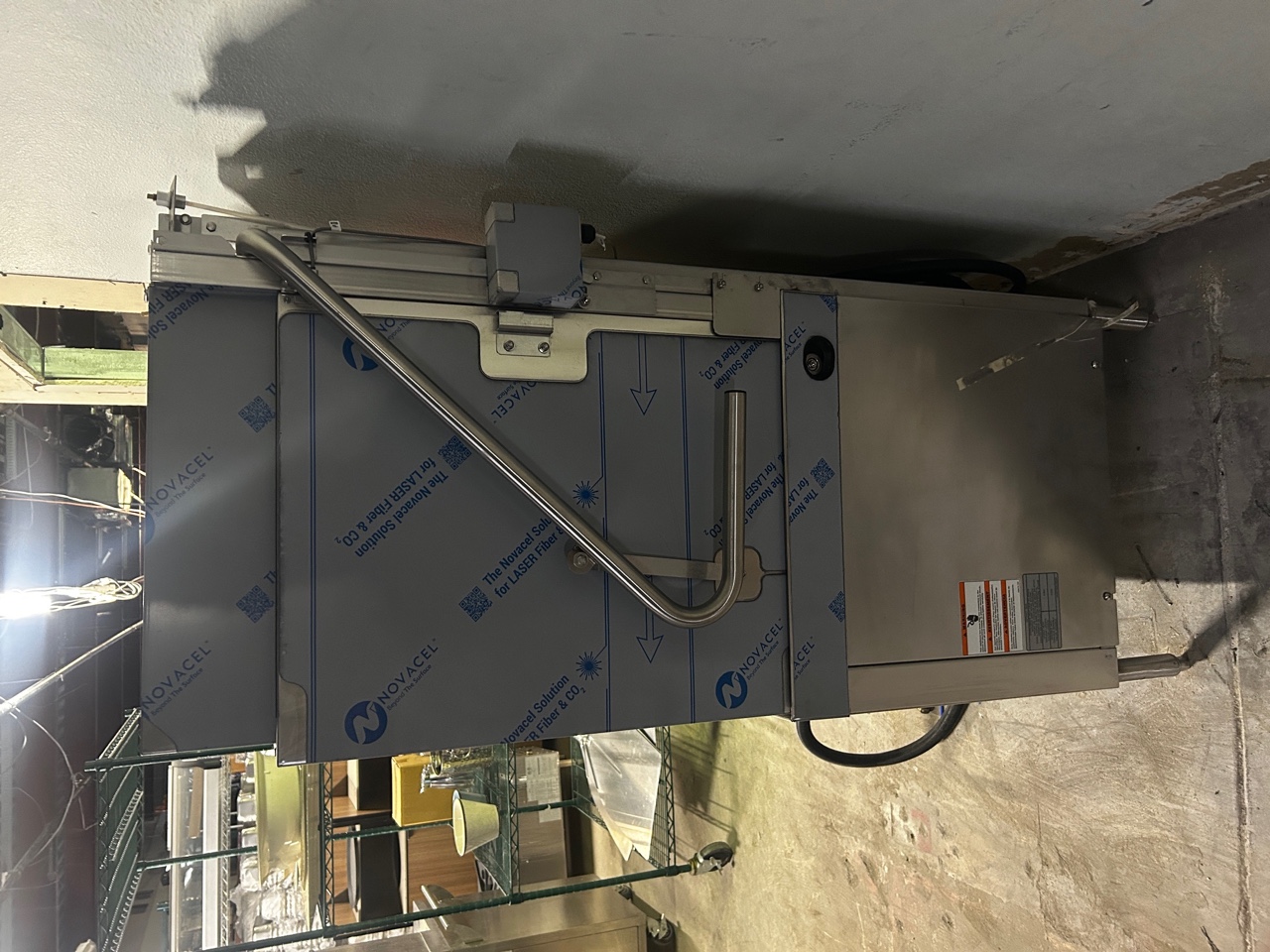 Side/rear view of Hobart AM16VLT-BAS ventless dishwasher showing door lift mechanism, warning label, and stainless steel construction with protective film intact