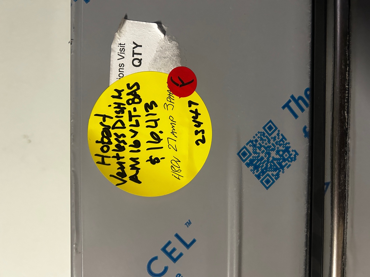Close-up of yellow handwritten label on Hobart dishwasher reading 'Hobart Ventless Dish M AM16VLT-BAS $16,413 480V 27 Amp 3-Phase 23447'