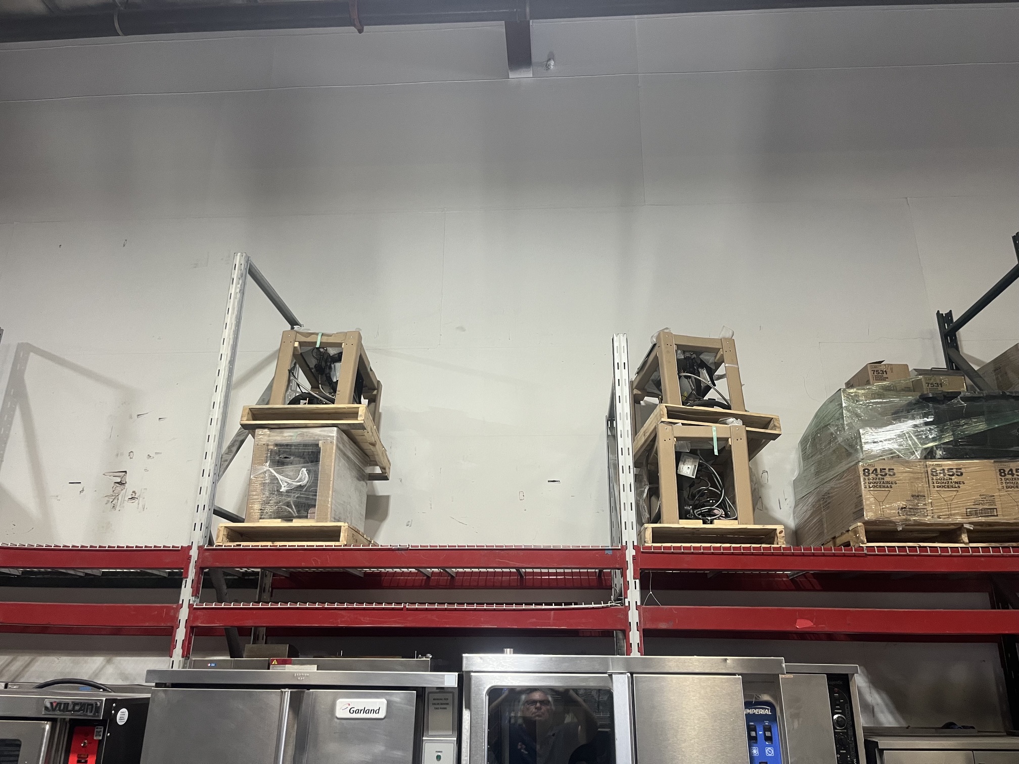 Two brand new Hatco HCSBF-24-F units in wooden shipping crates stored on warehouse shelving alongside other commercial kitchen equipment