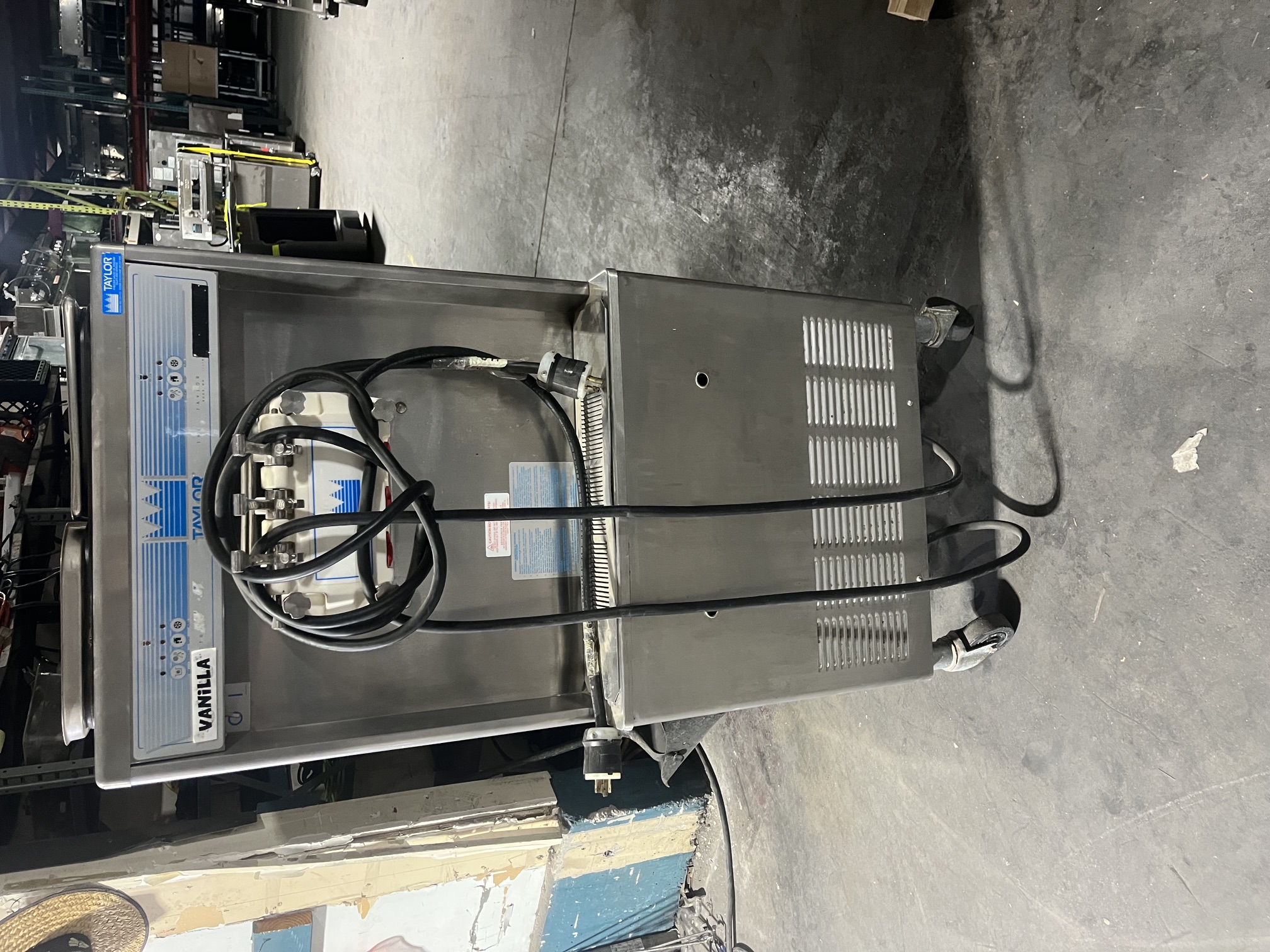 Front view of used Taylor 339-27 soft serve ice cream machine on casters with power cord wrapped around dispensing handles in warehouse setting