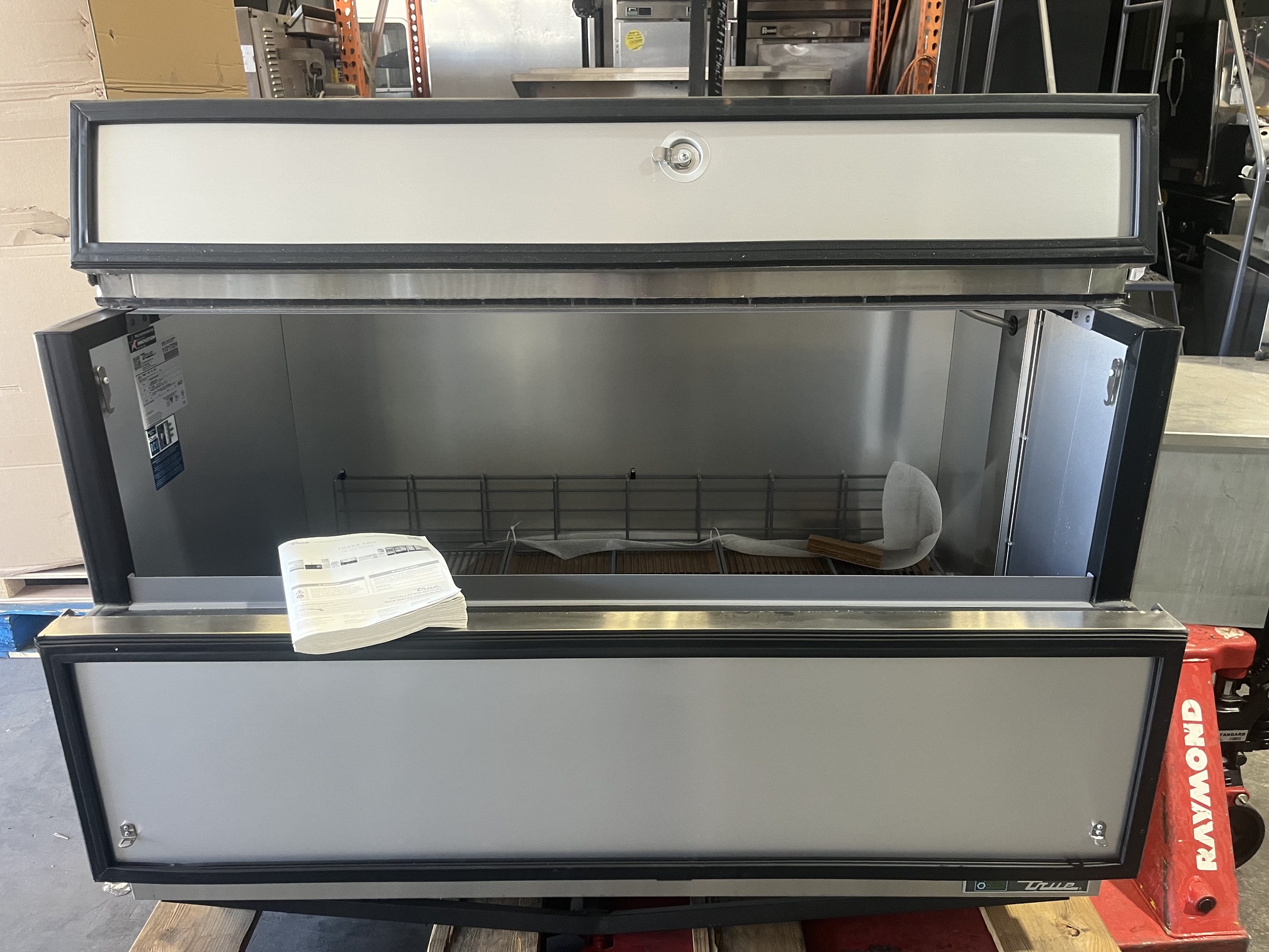 True TMC-58-S-HC milk cooler with flip-top lid open showing stainless steel interior, wire shelf, and included owner's manual