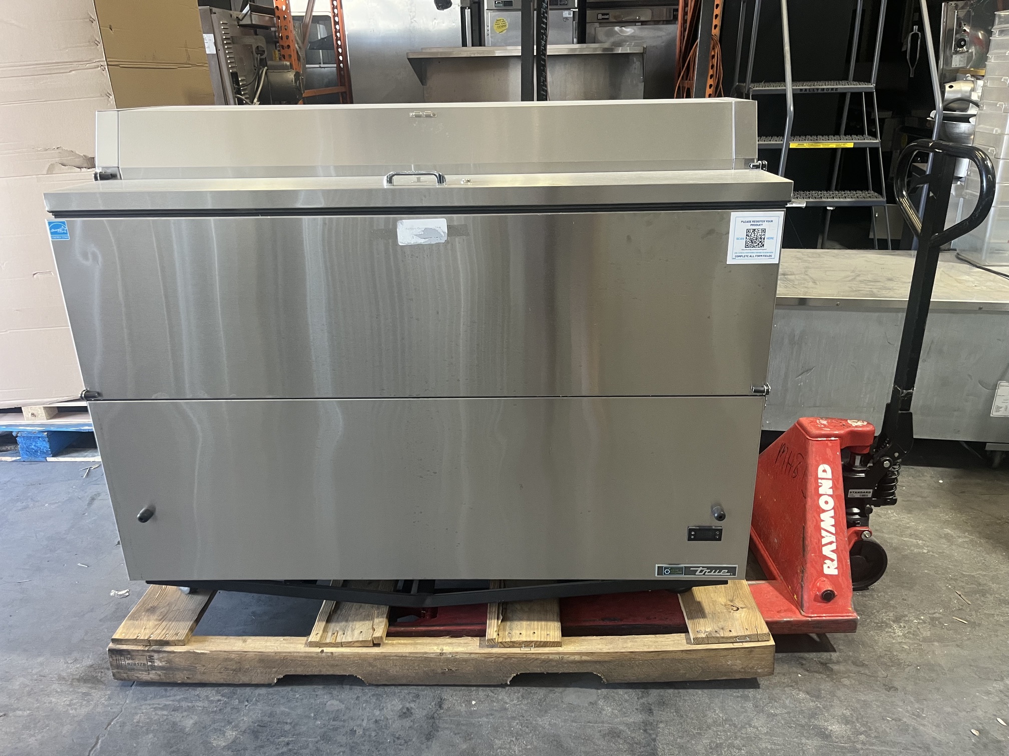 Rear view of brand-new True TMC-58-S-HC 58-inch milk cooler on pallet showing stainless steel exterior and True logo badge
