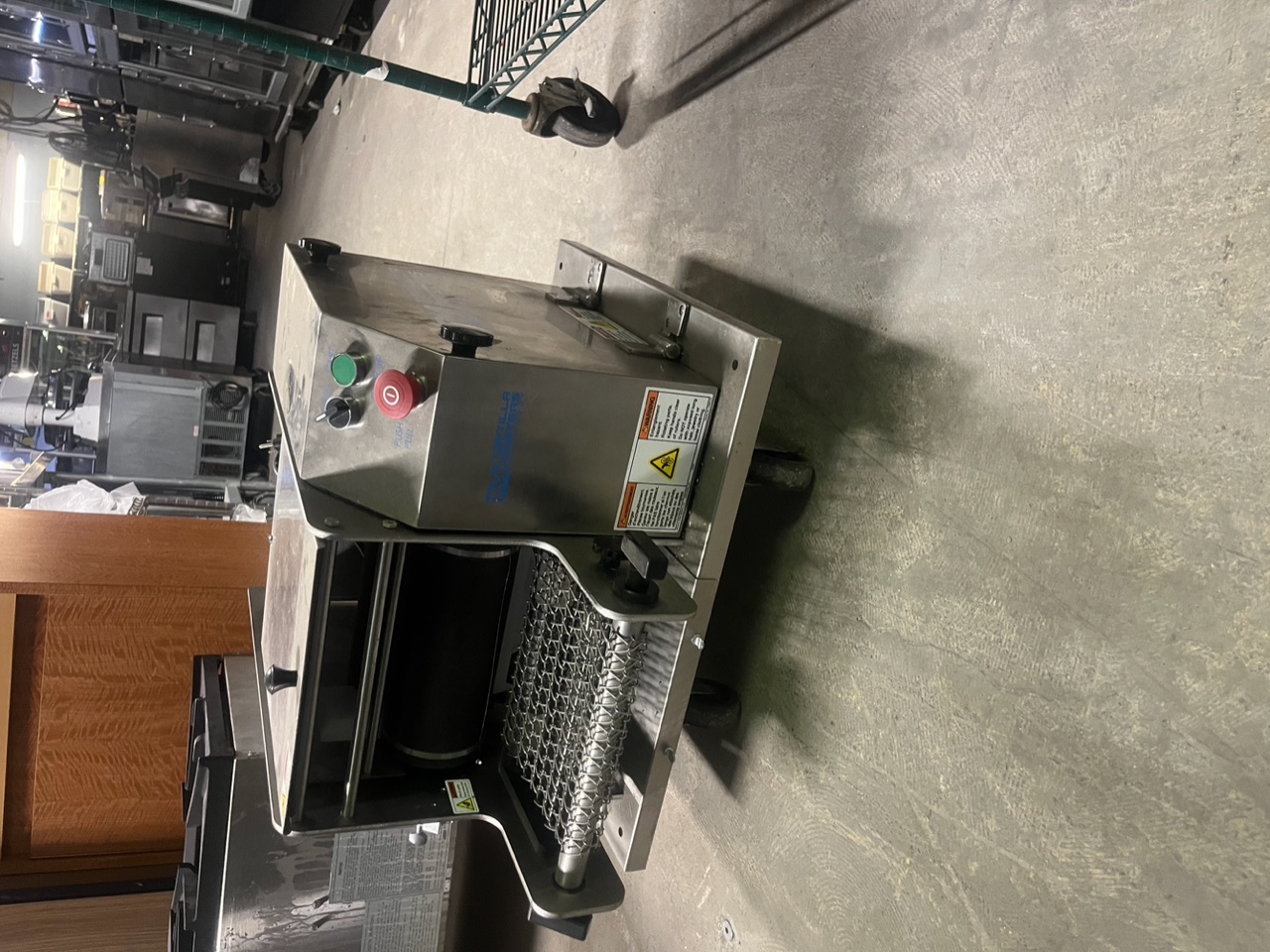 Front-angle view of the Tortilla Masters TM-105 Ventura Flex PL tortilla machine showing dough hopper, control buttons, and wire-mesh conveyor belt