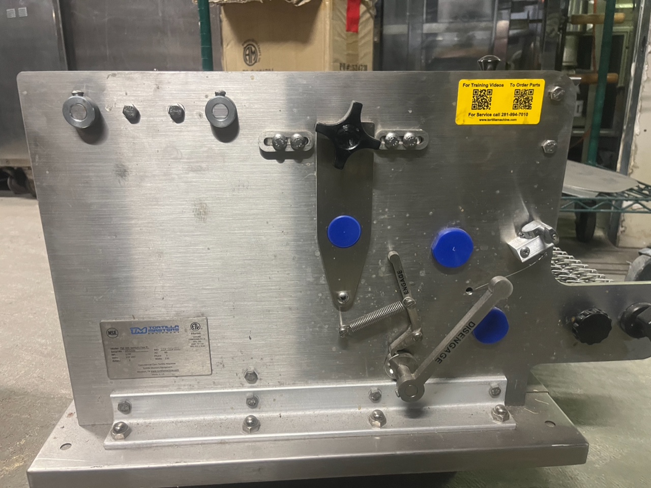 Rear panel of the Tortilla Masters TM-105 showing data plate, engage/disengage lever, service QR code sticker, and NSF/ETL certification labels